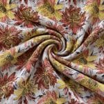 Ivory floral jacquard fabric gathered into a spiral of curved folds, showing oversized rust red and yellow flowers, dark grey leaves and gold-toned woven details.