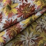 Close-up of folded floral jacquard fabric showing rust red and yellow flowers on an ivory front beside the contrasting olive-gold reverse with cream and burgundy floral motifs.