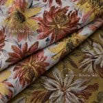 Ivory floral jacquard fabric in overlapping folds, with labels marking the right side with rust red and yellow flowers and the olive-gold reverse side with cream and burgundy floral motifs.