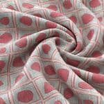 Close-up of geometric fabric in loose, rounded folds, showing raised-looking coral motifs framed by fine square outlines against a silver grey background.
