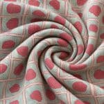 Silver grey and coral geometric fabric gathered into a spiral of curved folds, with irregular coral motifs within a repeating grid of outlined squares.