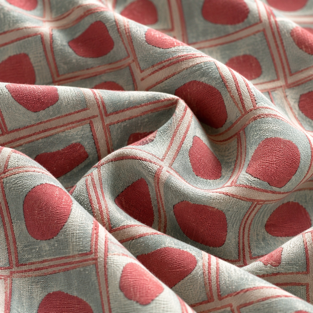 SKT1003-03 Geometric fabric arranged in soft overlapping folds, featuring irregular coral pink shapes inside a grid of fine coral double-lined squares on a silver grey background.
