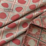 Silver grey and coral geometric fabric draped in overlapping folds, with a turned-back corner revealing the contrasting reverse side. White annotations identify the right and reverse sides.