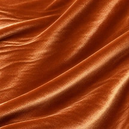 Copper orange crystal velvet fabric arranged in broad diagonal folds, revealing its smooth pile and reflective sheen.