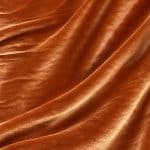 Copper orange crystal velvet fabric in gently overlapping diagonal folds, showing the lustrous finish and soft velvety texture.