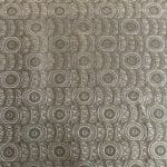 Close-up of sage green and silver grey jacquard fabric laid flat, featuring rows of concentric circular motifs alternating with narrow vertical bands of angular geometric shapes and subtle pale blue details.