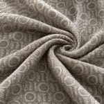 Geometric jacquard fabric gathered into a central spiral of folds, with repeating circular motifs and textured vertical bands in muted sage green and silver grey.