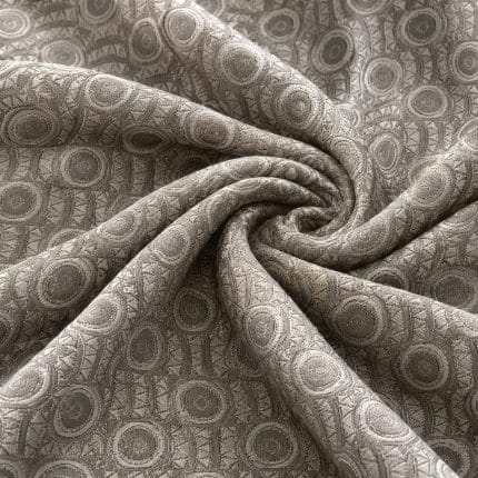 Geometric jacquard fabric gathered into a central spiral of folds, with repeating circular motifs and textured vertical bands in muted sage green and silver grey.