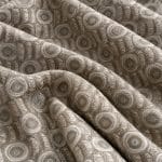 Sage green and silver grey jacquard fabric arranged in broad overlapping folds, showing raised concentric circles alternating with narrow vertical bands of angular geometric motifs.