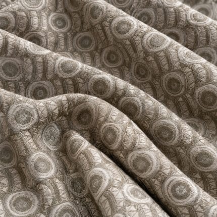 Sage green and silver grey jacquard fabric arranged in broad overlapping folds, showing raised concentric circles alternating with narrow vertical bands of angular geometric motifs.