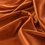 Close-up of copper orange Moroccan sablé fabric arranged in broad overlapping folds, with a warm sheen and smooth, finely textured surface.