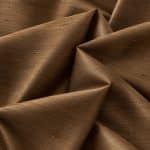 Copper-brown Dupion silk arranged in overlapping folds, showing the subtle horizontal slubs and shifting sheen on its textured right side.