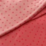 Soft pink silk jacquard folded diagonally, with the lighter right side above and the deeper reddish-pink reverse below, both showing small woven dot motifs.