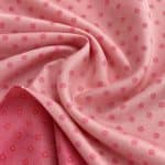 Pink jacquard fabric draped in loose folds, with small brighter pink dotted motifs and a turned-back edge revealing the deeper reddish-pink reverse side.