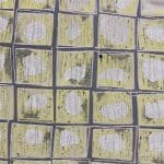 Flat view of geometric jacquard showing a regular grid of soft yellow squares bordered in grey, each containing an irregular pale beige oval, with textured dark flecks.
