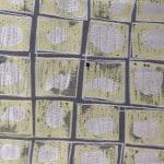 Close-up of geometric jacquard laid flat, displaying pale oval motifs on textured soft yellow squares separated by dark grey lines.
