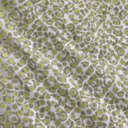 Close-up of silver-grey silk jacquard laid flat, showing densely repeating irregular circular motifs with lime green centres and grey-green outlines.