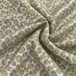 Silver-grey silk jacquard fabric gathered in soft folds, featuring repeating irregular circular motifs with textured lime green centres and grey-green outlines.
