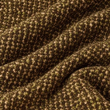 Textured wool fabric arranged in overlapping folds, with tightly clustered olive green, cream and brown yarn loops creating a raised, speckled surface on a dark brown ground.